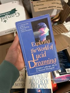 a person holding up a book about the world of lucid dreaming in front of boxes