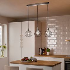 three lights hanging over a kitchen island with fruit on the counter and two chairs next to it