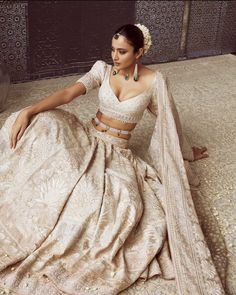 a woman sitting on the floor in a white and gold sari with her hands on her hips