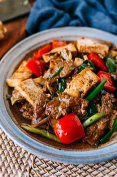 a plate filled with meat and vegetables on top of a woven place mat next to a wooden table