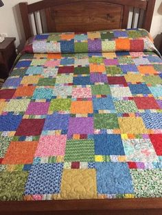 the bed is made with multicolored quilts and wooden headboard, along with two nightstands