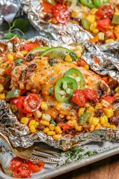 chicken and corn foil packets on a table with tomatoes, peppers, jalapenos, and avocado