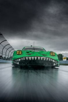 a green car with large teeth on it's head driving down a track in front of dark clouds