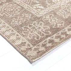 a beige rug with an intricate design on the top and bottom side, laying on a white floor