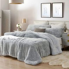 a bedroom with a large bed covered in grey blankets and pillows, along with two framed pictures on the wall