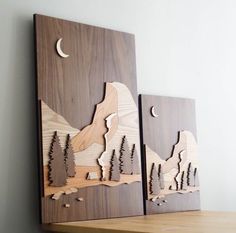 two wooden wall hangings with mountains and trees on them, one has a half moon in the sky