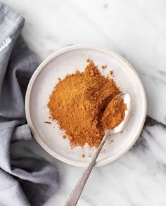 a white bowl filled with cinnamon powder and a spoon on top of it next to a gray napkin