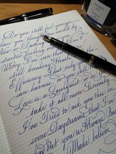 two fountain pens sitting on top of a notebook next to an ink bottle with writing on it