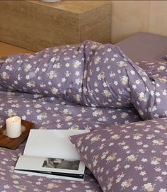 a bed with purple floral bedspread and white candle on it, next to an open book