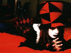 a woman laying on top of a bed wearing a red and black hat with long hair