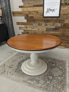 a round wooden table sitting on top of a rug in front of a wood paneled wall