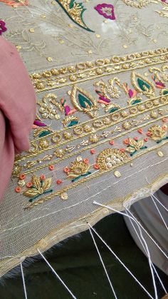 someone is working on an embroidered piece of cloth with gold and pink trimmings