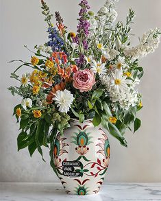 a vase filled with lots of flowers on top of a white countertop next to a wall