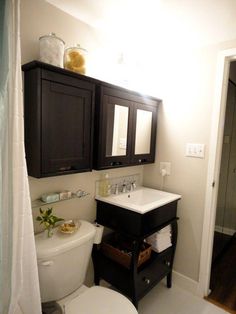 a white toilet sitting next to a sink in a bathroom under a vanity with two mirrors