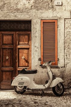 a white scooter parked in front of a building with shutters and wooden doors