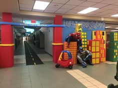 two children are playing in an indoor play area with colorful walls and flooring, while another child is sitting on a toy car