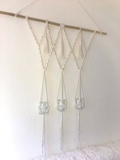 three hanging glass vases on a white wall next to a wooden stick and string