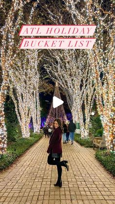 a woman is standing in the middle of a walkway with christmas lights on it and trees all around her