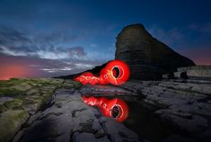 a red object sitting on top of a rock covered ground next to water at night