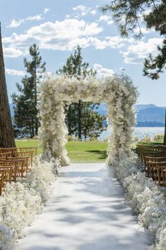 an outdoor ceremony setup with white flowers and greenery on either side of the aisle