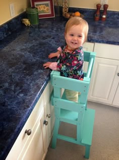 a toddler sitting in a high chair on top of a blue counter next to a sink