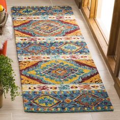 a multicolored area rug on the floor next to a potted plant