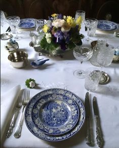 a blue and white dinner table setting with flowers in the center, silverware on the side