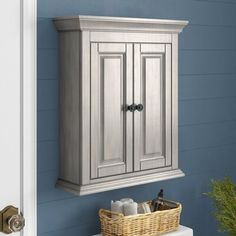 a bathroom cabinet with two doors and a basket on the sink counter next to it