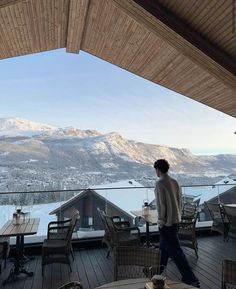 a man standing on top of a wooden deck next to a table and chair covered in snow