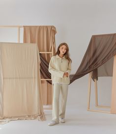 a woman standing in front of an empty room with curtains on the wall and behind her she is wearing white pants