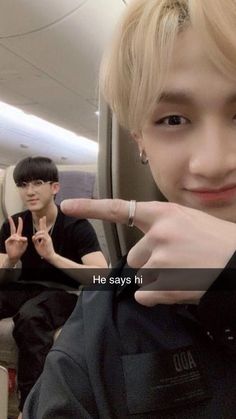 two young men sitting on an airplane and pointing at the camera with their fingers in the air