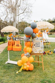 an orange and gray balloon arch is set up in the grass for a birthday party