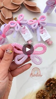 a person holding up some pink and purple hair clips on top of a white table