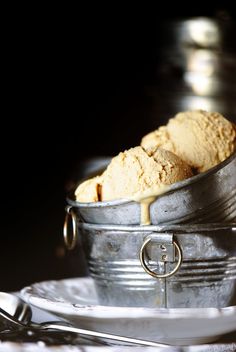 two scoops of ice cream sit in a metal bucket on a plate with silverware