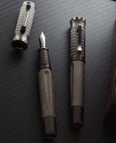 three fountain pens sitting on top of a table next to a pen and pencil case