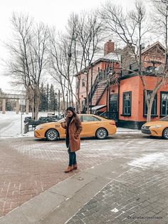 a woman standing on the sidewalk in front of two yellow cabs and some buildings