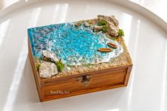 a small wooden box sitting on top of a white plate with rocks and water in it