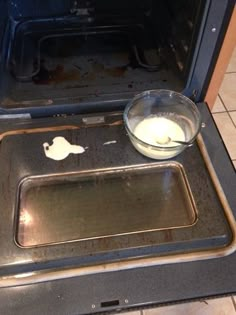 an open oven with something in it on the floor next to a bowl and pan