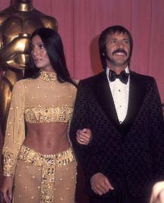 two people standing next to each other in front of an oscar statue and red carpet