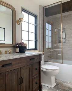 a white toilet sitting next to a bath tub in a bathroom under a window with a mirror