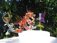 three colorful glass figurines sitting on top of a white table next to trees