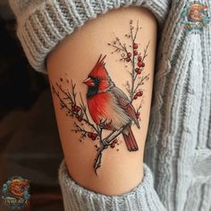 a woman's thigh with a red bird on it and berries around the leg