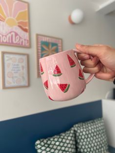 a person holding a pink coffee mug with watermelon designs on it in their hand