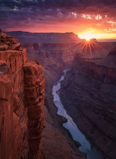 the sun is setting at the edge of a cliff overlooking a river and canyon below