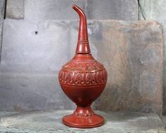 a red vase sitting on top of a stone slab