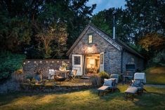 a small stone house is lit up at night with lights on the windows and patio furniture