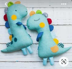 two stuffed dinosaurs sitting next to each other on top of a white wooden wall,