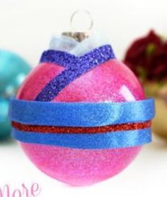 a pink ornament with blue and red ribbon on it sitting next to other ornaments