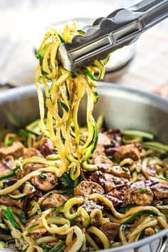 someone is lifting noodles out of a pan with meat and veggies in it