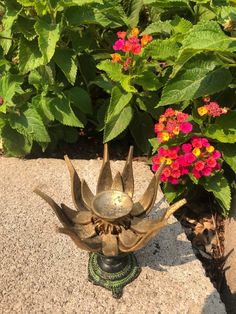 a metal flower pot sitting on top of a cement slab next to some colorful flowers